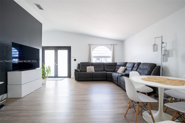 living room with wood finished floors, lofted ceiling, visible vents, and french doors