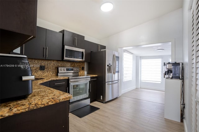 kitchen featuring light stone countertops, light wood-style floors, stainless steel appliances, baseboards, and decorative backsplash
