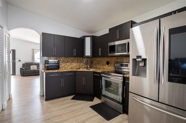 kitchen featuring decorative backsplash, lofted ceiling, a sink, light wood-style flooring, and appliances with stainless steel finishes