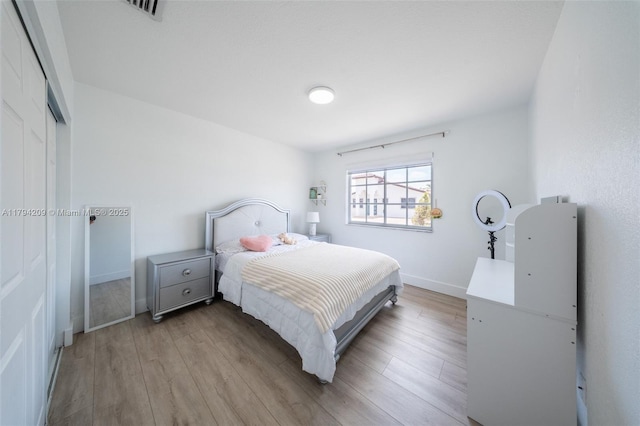 bedroom featuring baseboards, visible vents, wood finished floors, and a closet