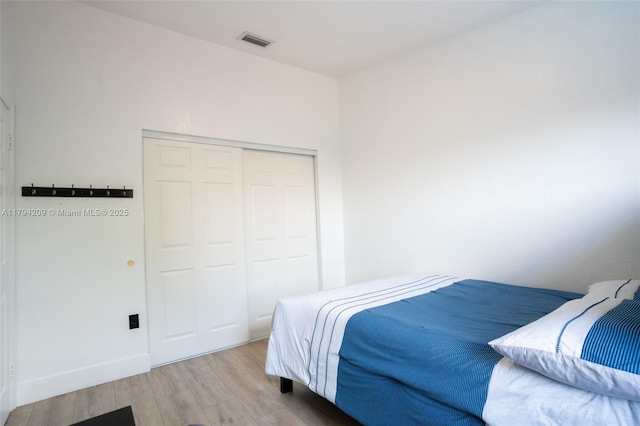 bedroom with baseboards, visible vents, wood finished floors, and a closet