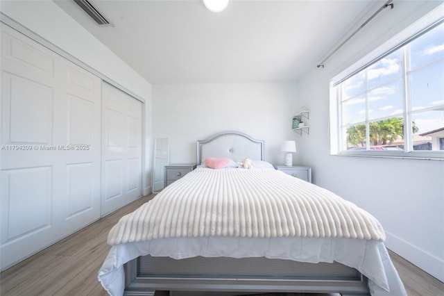 bedroom featuring light wood-type flooring, baseboards, visible vents, and a closet