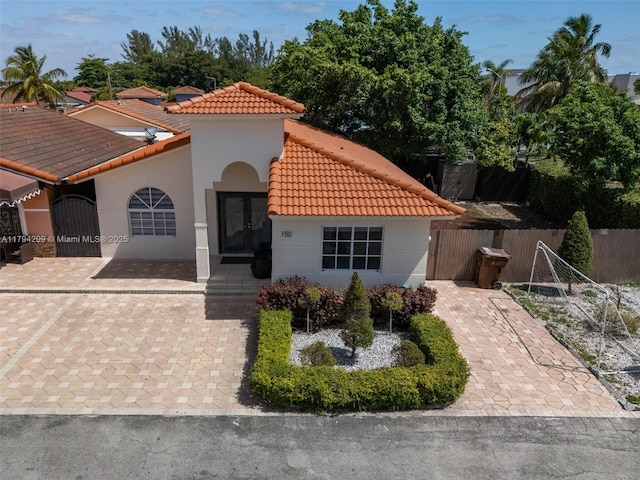 mediterranean / spanish-style house featuring french doors, a tile roof, a gate, fence, and stucco siding