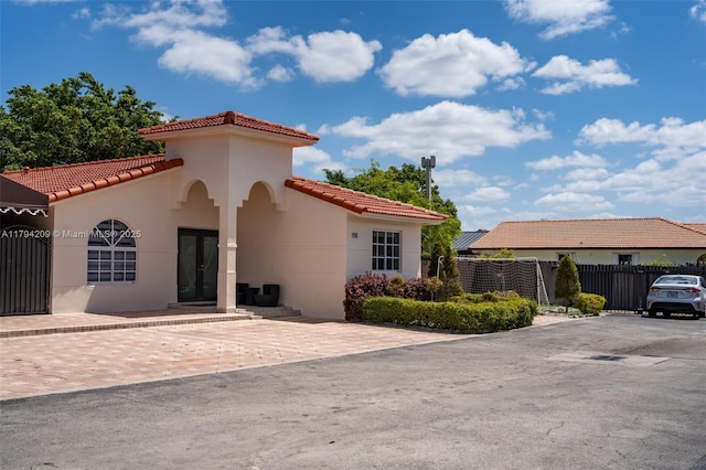 mediterranean / spanish-style home featuring a tiled roof, fence, french doors, and stucco siding