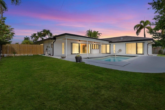 back of property at dusk featuring fence, stucco siding, a patio area, a lawn, and a ceiling fan
