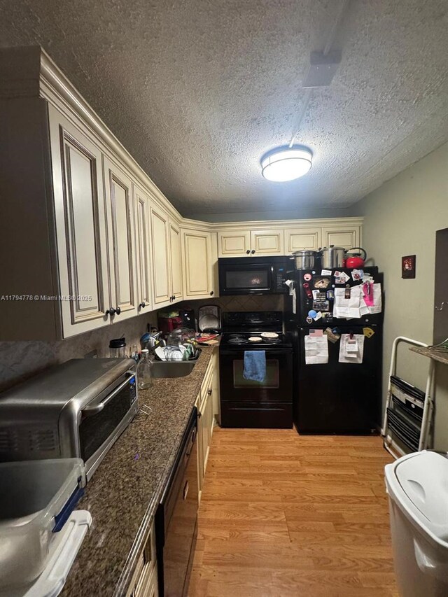 197 Kent L, West Palm Beach, FL 33417 - kitchen with black appliances, cream cabinets, light wood-style floors, a textured ceiling, and dark stone counters