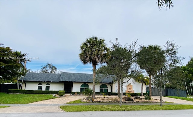 ranch-style home featuring fence, stucco siding, decorative driveway, and a front yard
