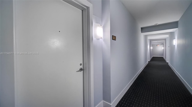 hall with baseboards and dark carpet