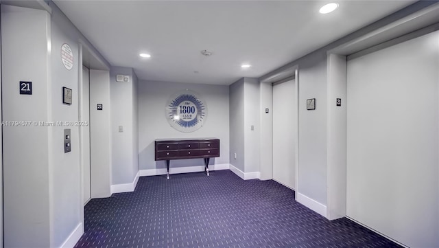 hallway featuring recessed lighting, baseboards, dark carpet, and elevator