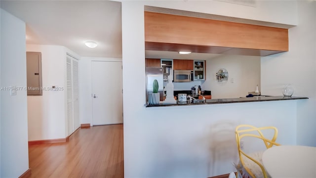 kitchen with brown cabinetry, dark countertops, appliances with stainless steel finishes, wood finished floors, and baseboards