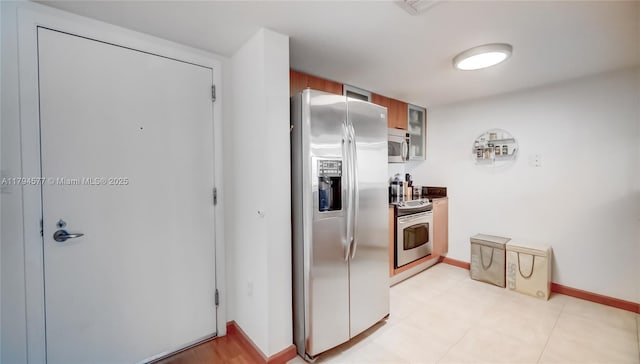 kitchen featuring brown cabinets, stainless steel appliances, baseboards, and glass insert cabinets