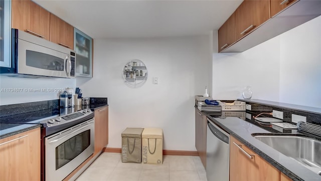 kitchen featuring light tile patterned floors, a sink, glass insert cabinets, dark stone counters, and stainless steel appliances