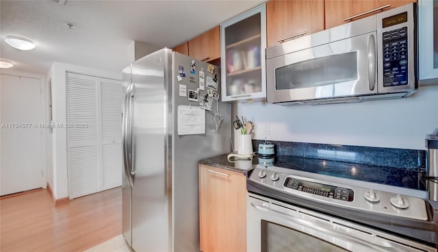 kitchen featuring glass insert cabinets, appliances with stainless steel finishes, light wood-style floors, and brown cabinets