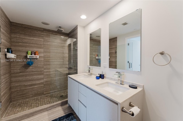 bathroom featuring a sink, a tile shower, double vanity, and visible vents