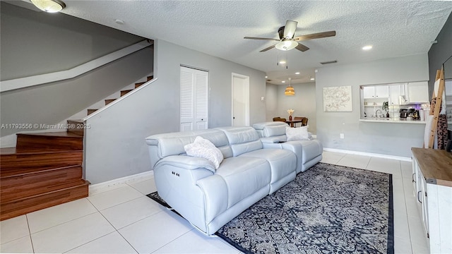 living room featuring a ceiling fan, a textured ceiling, visible vents, stairs, and light tile patterned flooring