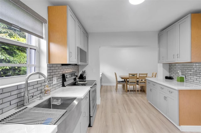 kitchen with tasteful backsplash, light wood-type flooring, a sink, light countertops, and stainless steel appliances
