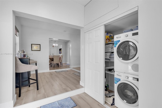 laundry area featuring laundry area, wood finished floors, stacked washing maching and dryer, baseboards, and a chandelier
