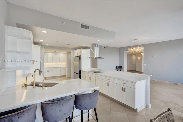 kitchen with visible vents, a sink, freestanding refrigerator, a peninsula, and wall chimney exhaust hood