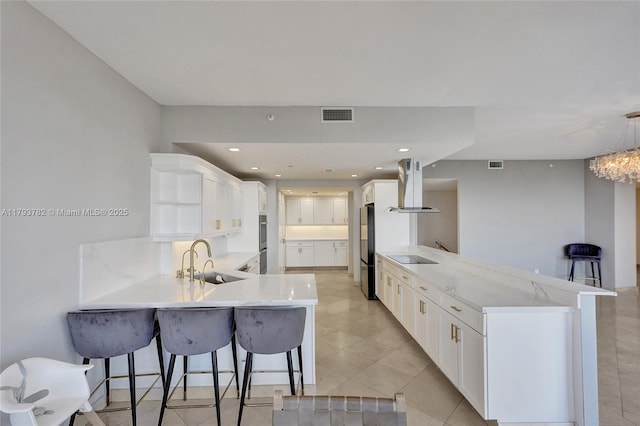 kitchen with visible vents, freestanding refrigerator, a peninsula, island exhaust hood, and a sink