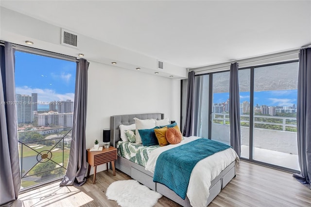bedroom featuring light wood-style floors, access to outside, a city view, and visible vents