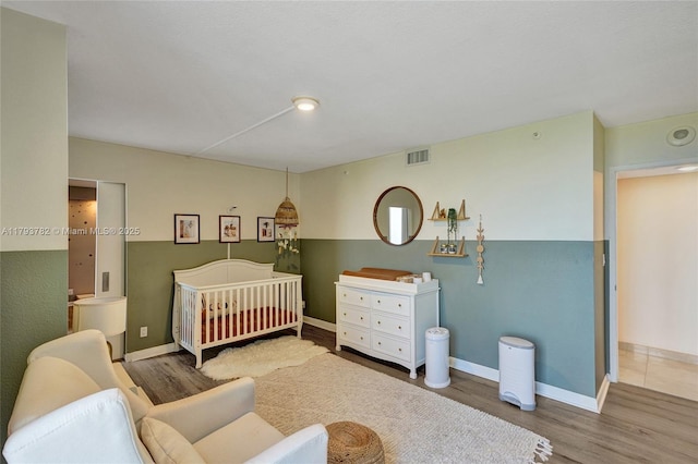 bedroom with baseboards, a nursery area, wood finished floors, and visible vents