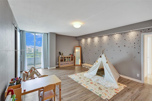 game room with baseboards, wood finished floors, baseboard heating, and expansive windows