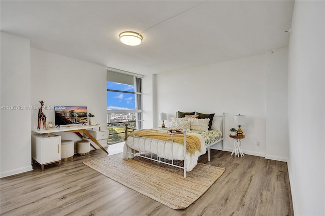 bedroom with baseboards, floor to ceiling windows, and wood finished floors