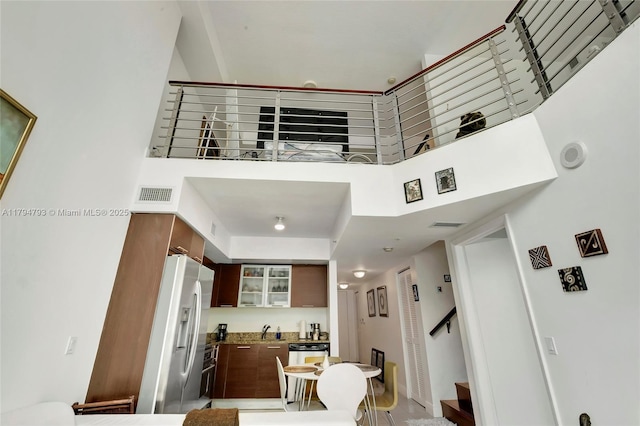 interior space featuring visible vents, glass insert cabinets, a high ceiling, fridge with ice dispenser, and a sink