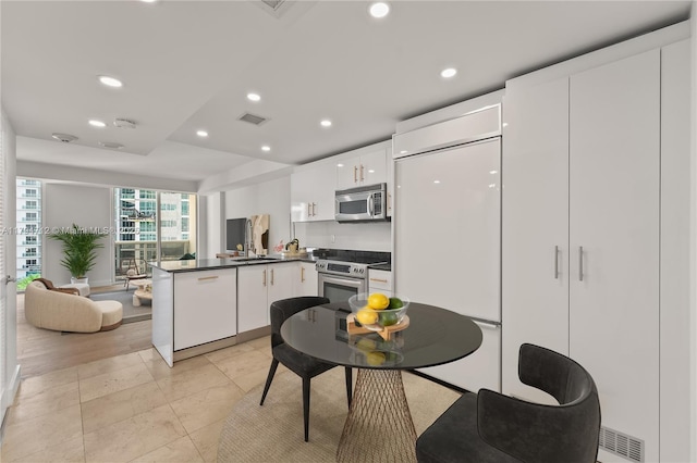 kitchen with visible vents, a peninsula, dark countertops, white cabinetry, and appliances with stainless steel finishes