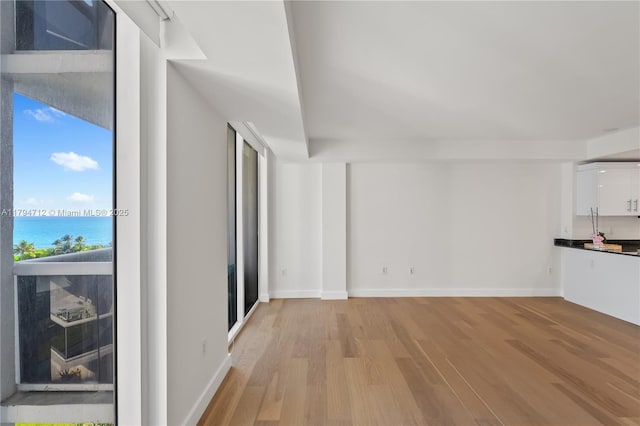 unfurnished living room with a water view, baseboards, and light wood-style floors