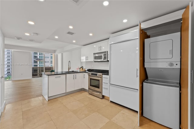 kitchen featuring dark countertops, stacked washer / drying machine, a sink, a peninsula, and stainless steel appliances