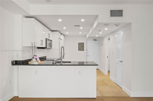 kitchen featuring white cabinets, a sink, a peninsula, stainless steel microwave, and visible vents