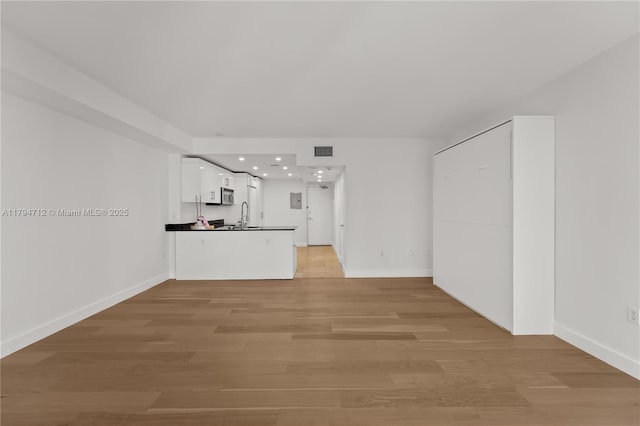 unfurnished living room featuring visible vents, baseboards, recessed lighting, a sink, and light wood-style flooring