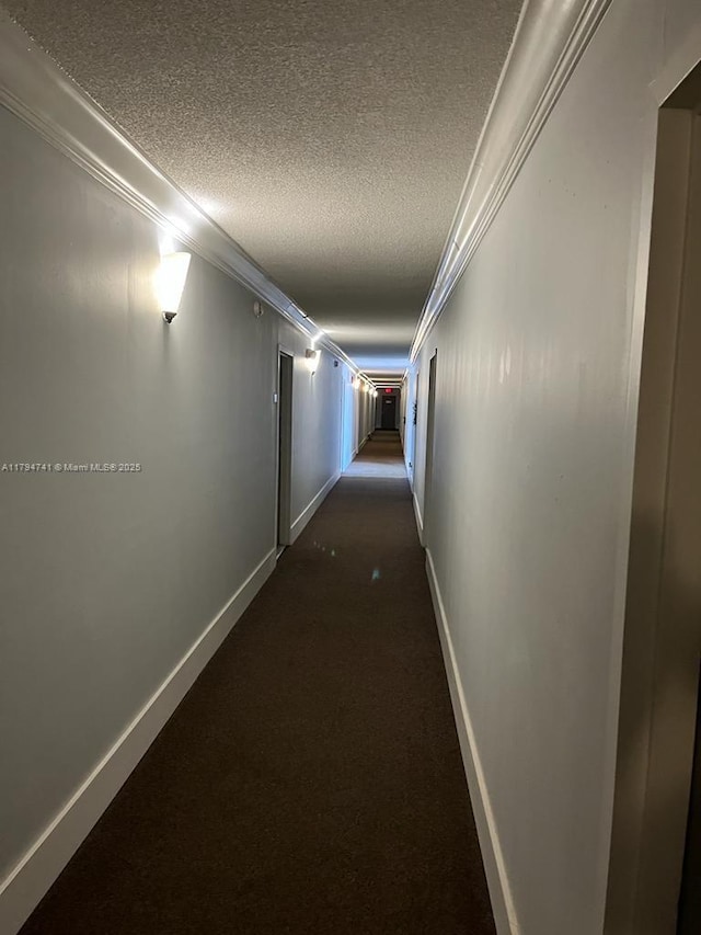 hall featuring baseboards, a textured ceiling, ornamental molding, and dark carpet