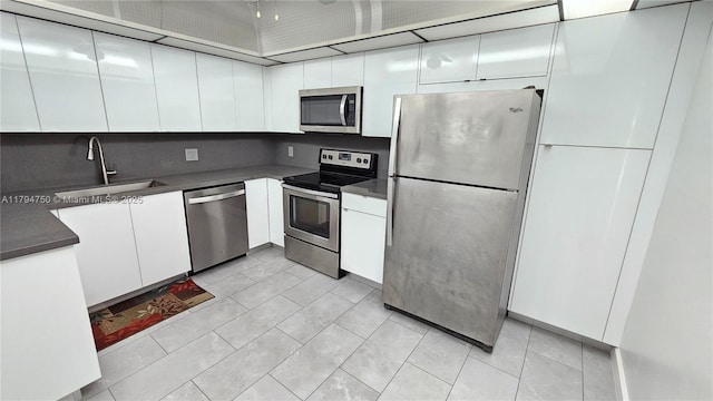kitchen with dark countertops, a sink, light tile patterned flooring, stainless steel appliances, and white cabinetry