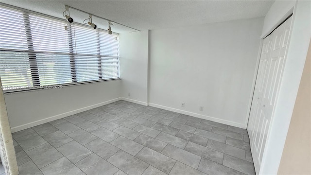 interior space with a textured ceiling, track lighting, baseboards, and a closet