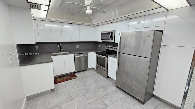 kitchen with white cabinets, dark countertops, appliances with stainless steel finishes, a sink, and a ceiling fan