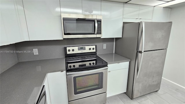 kitchen with light tile patterned flooring, baseboards, modern cabinets, white cabinetry, and appliances with stainless steel finishes