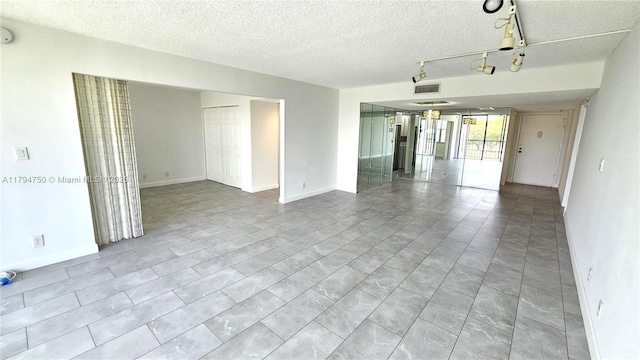 empty room with track lighting, baseboards, a textured ceiling, and visible vents