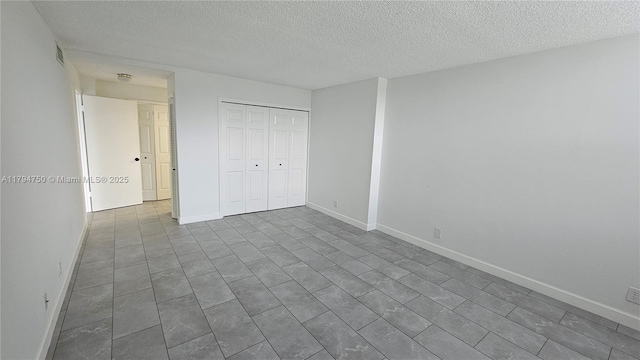 unfurnished bedroom featuring visible vents, a textured ceiling, a closet, and dark tile patterned flooring
