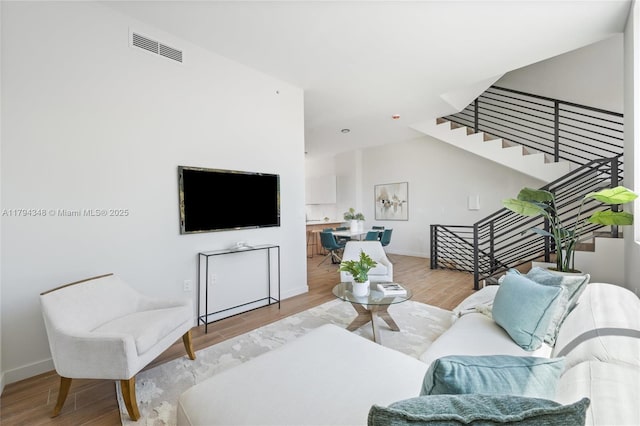 living area featuring baseboards, light wood finished floors, stairs, and visible vents