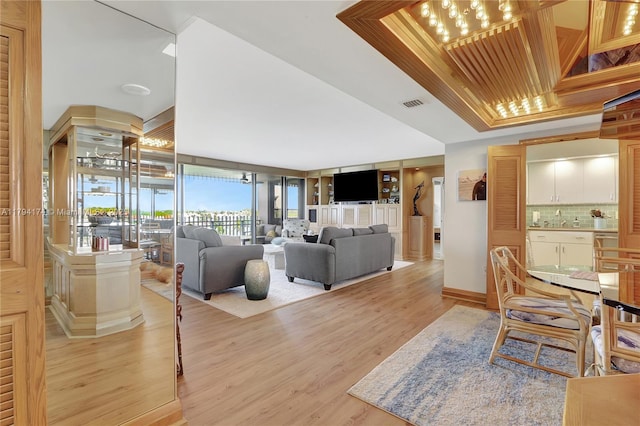living room with a tray ceiling, visible vents, and light wood-type flooring