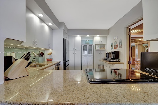kitchen with a sink, light stone counters, tasteful backsplash, and stovetop