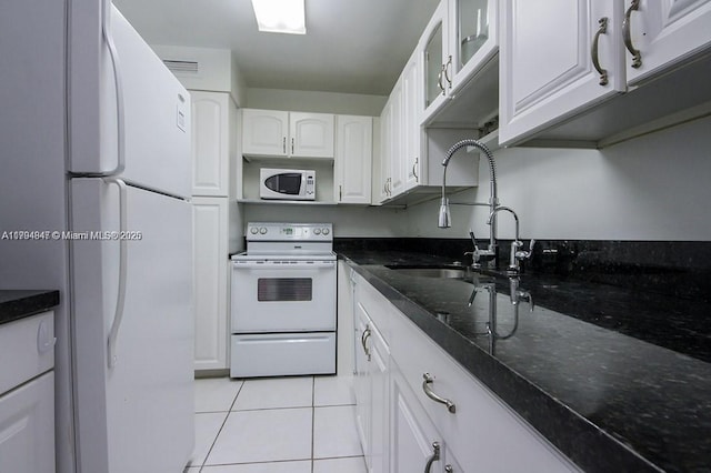 kitchen with light tile patterned flooring, white appliances, dark stone counters, white cabinetry, and a sink