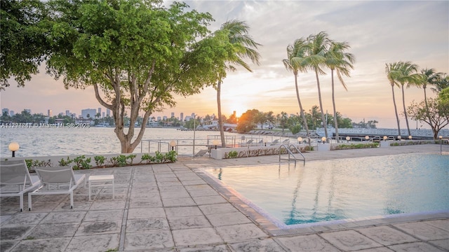 pool at dusk with a patio and a water view