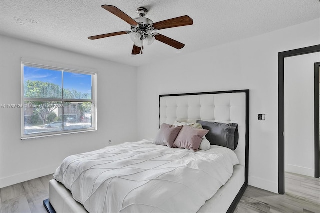 bedroom featuring light wood-type flooring, a ceiling fan, a textured ceiling, and baseboards