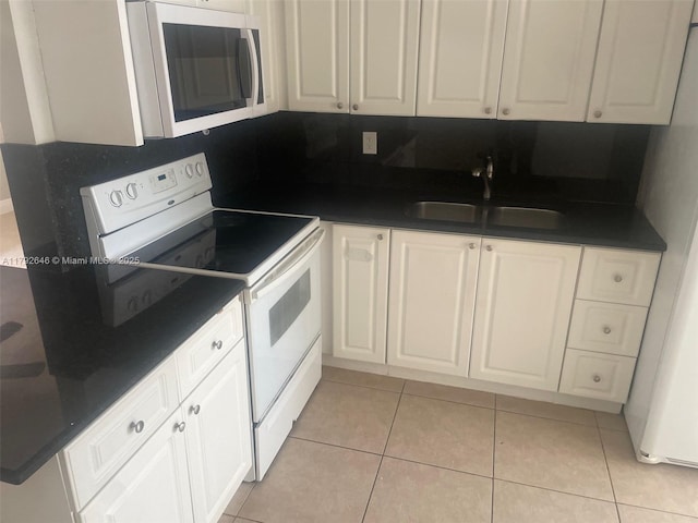 kitchen featuring a sink, dark countertops, white appliances, and white cabinetry