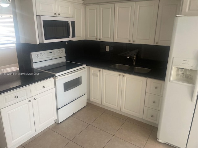 kitchen featuring dark countertops, white appliances, white cabinets, a sink, and light tile patterned floors