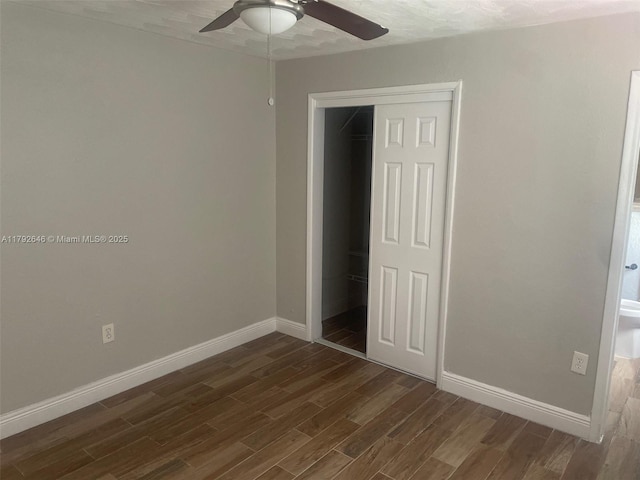 unfurnished bedroom featuring baseboards, a ceiling fan, a closet, and dark wood-type flooring