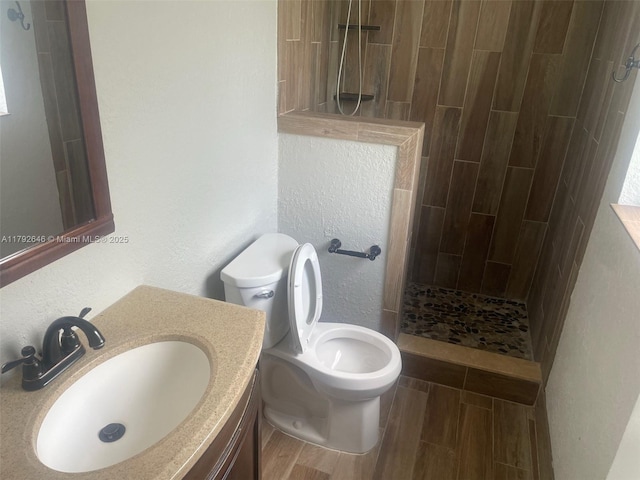 full bathroom with wood finished floors, a walk in shower, vanity, toilet, and a textured wall